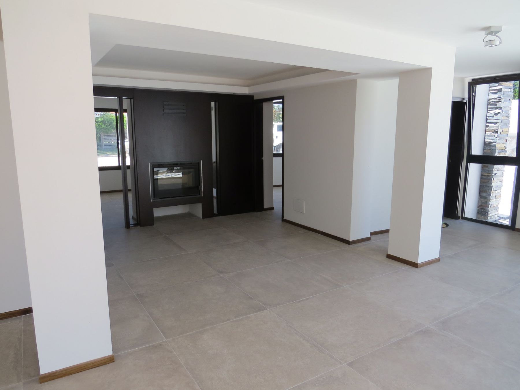 En la fotografía se ve la entrada a los consultorios, que encierran una estufa de alto rendimiento entre ellas. Es un espacio amplio con piso de porcelanato y se puede apreciar una ventana, a través de la cual se ve una pared revestida en piedra.